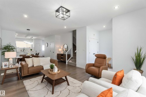 Open-concept living space featuring wood-finish flooring, recessed lighting, a contemporary ceiling fixture, and a staircase with white balusters - 124 28 Street, Edmonton, AB 