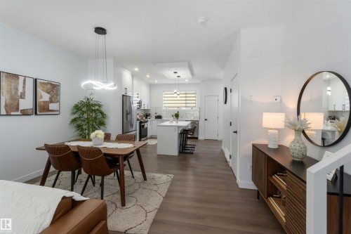 Open-concept living area featuring wood-finish flooring, a modern kitchen with white cabinetry and a central island, and a dining space illuminated by a contemporary pendant light fixture - 124 28 Street, Edmonton, AB 
