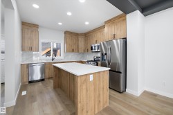 Contemporary kitchen featuring a central island with white countertop, stainless steel appliances, light wood-finish cabinetry, and recessed lighting - 
