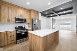 Open-concept kitchen featuring wood-finish cabinetry, stainless steel appliances, and white stone countertops - 
