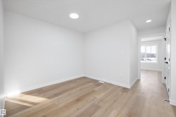 Bright interior room featuring wood-finish flooring, recessed lighting, white baseboards, and a white interior door with black hardware - 