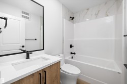 Bathroom featuring a wood-finish vanity with a white countertop and integrated sink, matte black faucet, and a large rectangular mirror - 