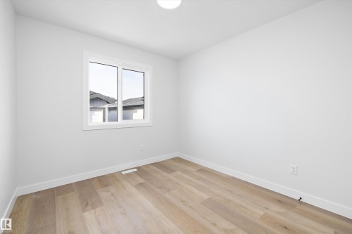 Bright interior space featuring a window with white trim, light-toned wood-finish flooring, white walls, white baseboards, and a flush-mount ceiling light - 954 Elderberry Landing, Edmonton, AB - Indoor Photo Showing Other Room