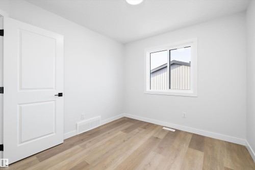 Light-filled room featuring durable wood-finish flooring, a white interior door with matte black hardware, and a single window offering natural light - 954 Elderberry Landing, Edmonton, AB - Indoor Photo Showing Other Room