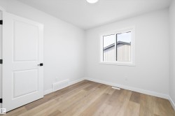 Light-filled room featuring durable wood-finish flooring, a white interior door with matte black hardware, and a single window offering natural light - 