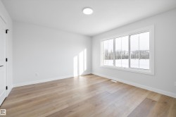 Spacious room featuring light wood-finish flooring, a contemporary flush-mount ceiling light, white baseboards, and a large multi-pane window with white trim - 