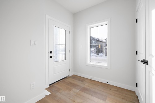 Entryway featuring a white paneled door with glass inserts and matte black hardware, wood-finish flooring, a white trim window, and white baseboards - 954 Elderberry Landing, Edmonton, AB - Indoor Photo Showing Other Room