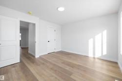 Spacious room featuring wood-finish flooring, white walls, and bright overhead lighting - 