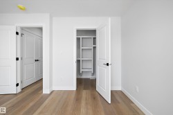 Spacious room featuring wood-finish flooring, white walls, and a built-in closet with shelving - 