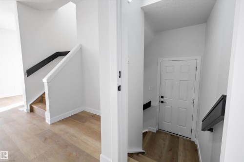 Split-level entry featuring light wood-finish flooring, white trim, white walls, white paneled door, and black metal handrails - 954 Elderberry Landing, Edmonton, AB - Indoor Photo Showing Other Room