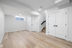 Spacious room featuring light wood-finish flooring, white walls, and a large egress window - 