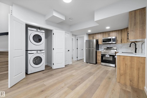 Modern kitchen featuring wood-finish cabinetry, stainless steel appliances, and a marble-finish backsplash - 954 Elderberry Landing, Edmonton, AB - Indoor Photo Showing Laundry Room