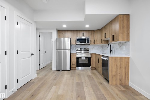 Kitchen featuring wood-finish cabinetry, stainless steel appliances, white countertops, and a white tile backsplash - 954 Elderberry Landing, Edmonton, AB - Indoor Photo Showing Kitchen With Stainless Steel Kitchen