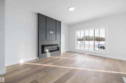 Spacious room featuring a modern fireplace wall with panel detailing, light wood-finish flooring, a large multi-pane window, white walls, and a recessed ceiling light fixture - 