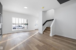 Open-concept living space featuring wood-finish flooring, a large multi-pane window, and a modern staircase with a black handrail - 