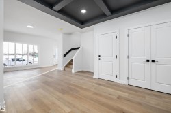 Spacious interior featuring a coffered ceiling with recessed lighting, wide plank wood-finish flooring, and white paneled doors with matte black hardware - 