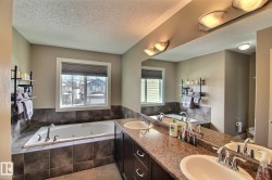 Spacious bathroom featuring a large jetted bathtub with tiled surround, a vanity with dual sinks, and a large mirror with integrated lighting - 