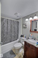 The bathroom features a bathtub with a shower, a toilet, and a vanity with a granite countertop and a wood cabinet - 