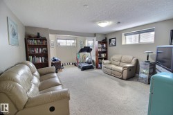 The expansive carpeted living space features a ceiling light fixture, wall-mounted light fixtures, and two windows with blinds - 