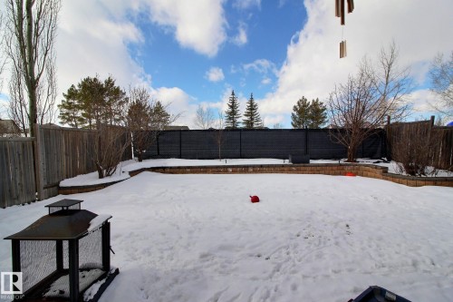 The property features a fenced yard with a snow-covered lawn, mature trees, and a brick retaining wall - 1212 Westerra Crescent, Stony Plain, AB - Outdoor