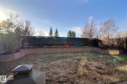 Expansive yard featuring a tiered retaining wall system with stone blocks, established landscaping beds, a combination of wood panel fencing and chain-link fencing, and mature trees - 