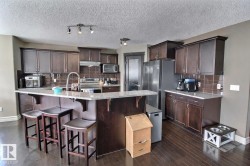 This kitchen features dark wood cabinetry, stainless steel appliances, a center island with bar seating, and a light-colored granite countertop - 