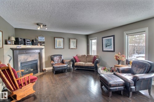 This inviting living area features dark wood flooring, a fireplace with a stone surround and mantel, and windows that provide natural light - 1212 Westerra Crescent, Stony Plain, AB - Indoor Photo Showing Living Room With Fireplace