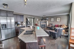 The property features a kitchen with dark cabinetry, stainless steel appliances, and a granite island with an undermount sink, which opens to a living area with dark wood flooring and a fireplace - 