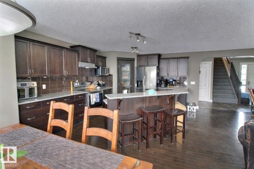 Well-appointed kitchen featuring dark wood cabinetry, stainless steel appliances, a tiled backsplash, and a breakfast bar with seating - 1212 Westerra Crescent, Stony Plain, AB - Indoor Photo Showing Kitchen With Upgraded Kitchen