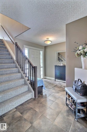 This inviting foyer features durable tile flooring, a carpeted staircase with a dark wood railing, and a front entry door with side light windows - 1212 Westerra Crescent, Stony Plain, AB - Indoor Photo Showing Other Room