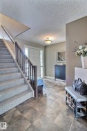 This inviting foyer features durable tile flooring, a carpeted staircase with a dark wood railing, and a front entry door with side light windows - 