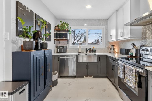 This kitchen features a combination of white upper cabinets and dark lower cabinets, a stainless steel farmhouse sink, and a patterned backsplash - 7408 92 Avenue, Edmonton, AB - Indoor Photo Showing Kitchen With Double Sink With Upgraded Kitchen