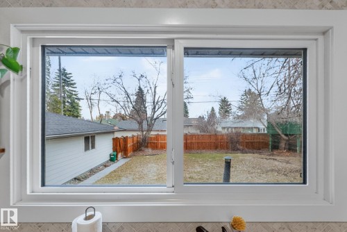 View of the backyard featuring a wooden fence and trees, framed by a white-trimmed window - 7408 92 Avenue, Edmonton, AB - Indoor Photo Showing Other Room