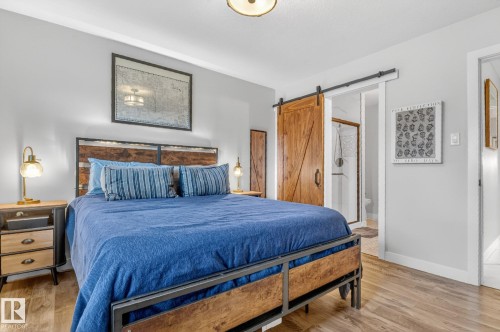 This bedroom features wood-look flooring, a sliding barn door, and a clear glass shower enclosure visible through the doorway - 7408 92 Avenue, Edmonton, AB - Indoor Photo Showing Bedroom