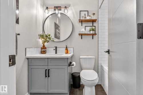 The bathroom features a grey vanity with a white countertop and a circular mirror with an industrial-style light fixture - 7408 92 Avenue, Edmonton, AB - Indoor Photo Showing Bathroom