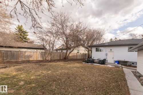 The property features a spacious rear yard with a lawn, mature trees, and a wooden fence along the perimeter - 7408 92 Avenue, Edmonton, AB - Outdoor