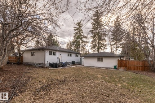 The property features a white exterior, a dark roof, and a detached garage, all surrounded by various trees - 7408 92 Avenue, Edmonton, AB - Outdoor
