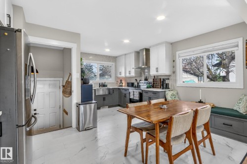The kitchen features white upper cabinetry, gray lower cabinetry, a stainless steel sink, and a window providing natural light - 7408 92 Avenue, Edmonton, AB - Indoor