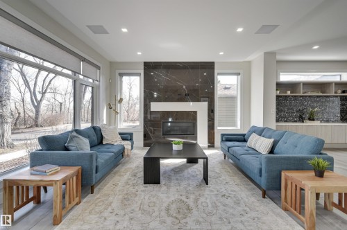 Modern living area with expansive window walls, a linear fireplace set within a dark stone slab surround, recessed lighting, and light wood-finish flooring - 9741 90 Avenue, Edmonton, AB - Indoor Photo Showing Living Room With Fireplace