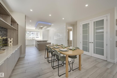 Open-concept living space featuring wood-finish flooring, built-in shelving with integrated cabinetry, and white double doors with frosted glass panels - 9741 90 Avenue, Edmonton, AB - Indoor