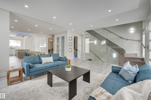 Open-concept living space featuring wood-finish flooring, recessed lighting, and a glass-paneled staircase with a metal handrail - 9741 90 Avenue, Edmonton, AB - Indoor Photo Showing Living Room