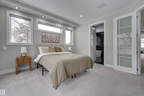 Spacious room featuring multiple windows, recessed lighting, light-colored carpet flooring, a white glass-paneled door, and an open doorway revealing a bathroom with dark tiled walls and a white freestanding tub - 9741 90 Avenue, Edmonton, AB - Indoor Photo Showing Bedroom