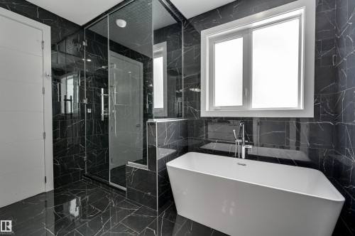 Contemporary bathroom featuring a freestanding tub, glass-enclosed shower, black marble-look tiling, chrome fixtures, and a white framed window - 9741 90 Avenue, Edmonton, AB - Indoor Photo Showing Bathroom