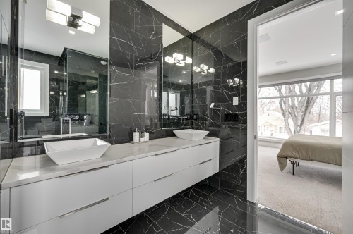 Bathroom featuring full-height black marble-look wall and floor tiling, a long white floating vanity with double vessel sinks, and a large mirror extending to the ceiling - 9741 90 Avenue, Edmonton, AB - Indoor Photo Showing Bathroom