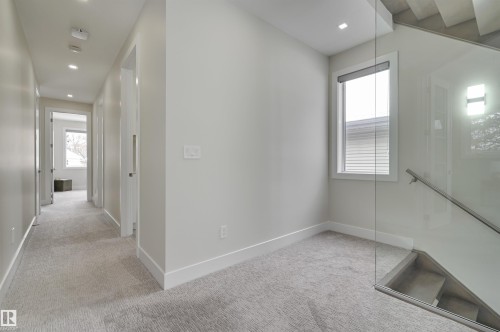 Carpeted hallway with recessed lighting and multiple doorways, featuring a glass-panel staircase with a metal handrail - 9741 90 Avenue, Edmonton, AB - Indoor Photo Showing Other Room