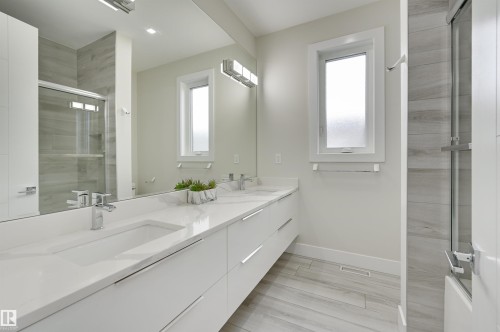 Dual vanity with integrated sinks, white cabinetry, chrome fixtures, and a large mirror - 9741 90 Avenue, Edmonton, AB - Indoor Photo Showing Bathroom