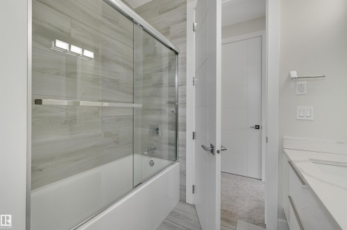Bathroom featuring a white tub with sliding glass doors, light-toned wood-finish tile surround, and a vanity with a white countertop - 9741 90 Avenue, Edmonton, AB - Indoor Photo Showing Bathroom