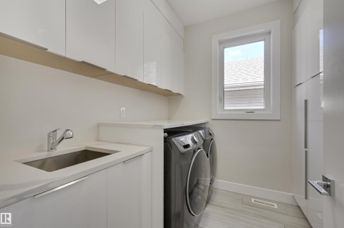 Laundry area featuring white cabinetry, a built-in sink with a chrome faucet, a light-colored countertop, and a window - 9741 90 Avenue, Edmonton, AB - Indoor Photo Showing Laundry Room