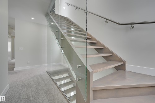 Modern staircase featuring light-toned treads, clear glass railing, and a stainless steel handrail - 9741 90 Avenue, Edmonton, AB - Indoor Photo Showing Other Room