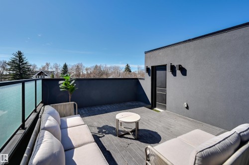 Rooftop terrace featuring composite decking, frosted glass railings, a dark stucco exterior wall, and exterior lighting fixtures - 9741 90 Avenue, Edmonton, AB - Outdoor With Exterior